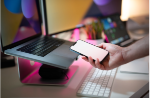 A person using a smartphone alongside a laptop, representing the crafting of customized advocacy messages to boost engagement.