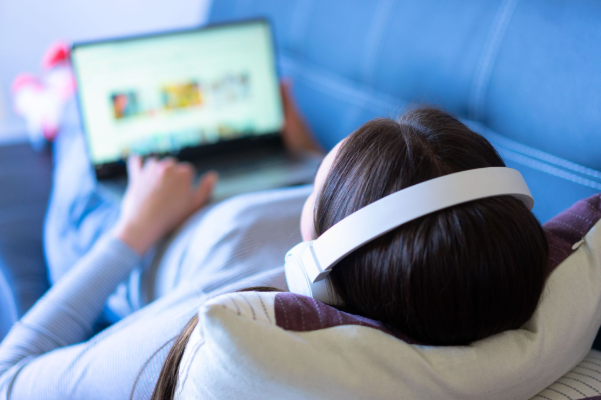 From live scores to streaming: the digital transformation of football Over-the-shoulder shot of a woman wearing white headphones lying back on a sofa while using a laptop.